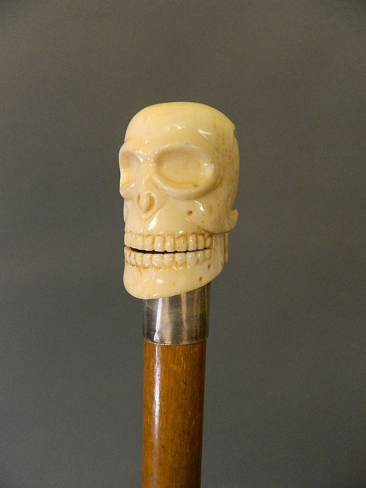 A bone handled walking stick with silver collar and carved skull handle