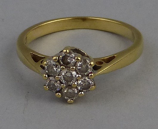 A diamond cluster ring, comprising seven stones claw set as a flowerhead (0