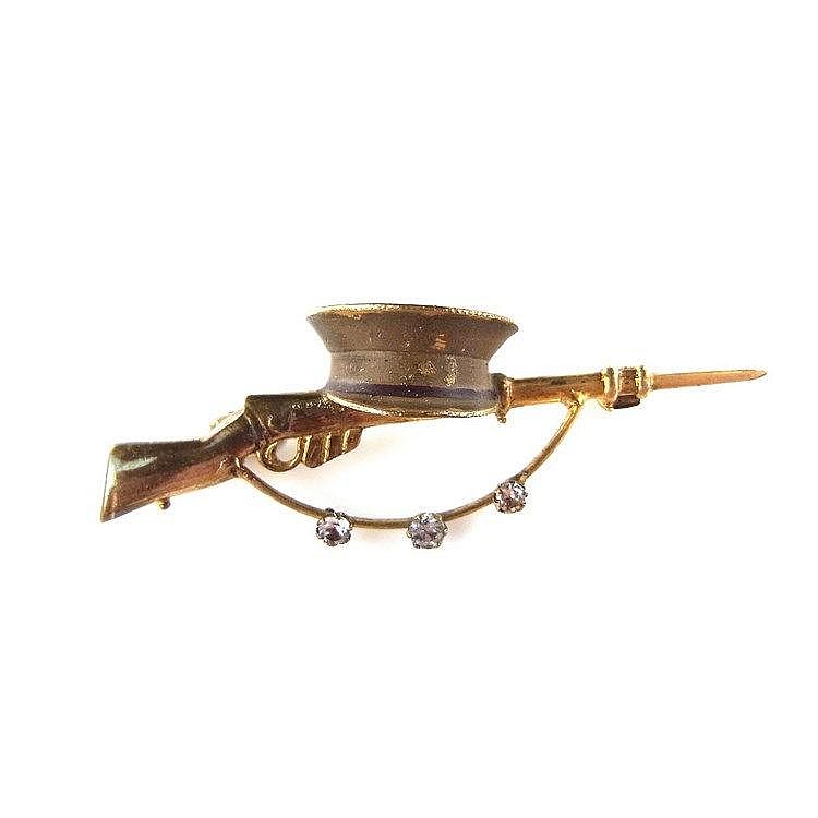 Yellow metal rifle and hat brooch. With three paste accents. Length 50 mm.